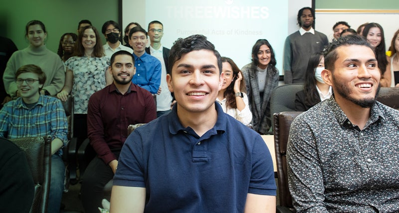 A student sits in a Mason classroom among his peers and smiles.