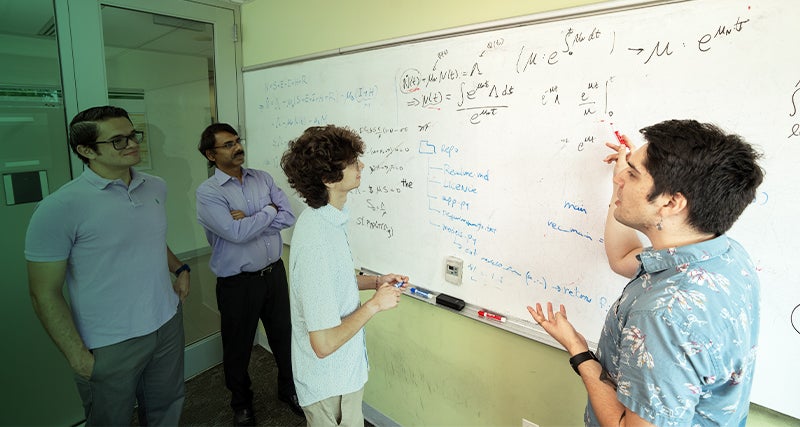 A young student works out equations on a whiteboard with the help of a student teacher