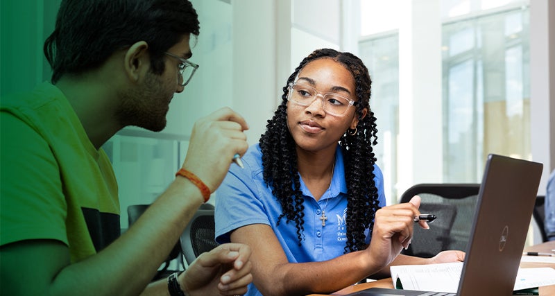 A pair of Mason students work together on a laptop and workbook