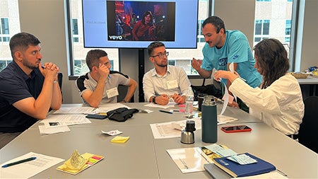 4 people seated at a table with one standing in conversation