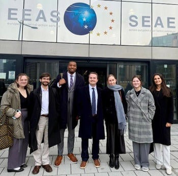 A group of people stand outside of a building that says EEAS on the sign.