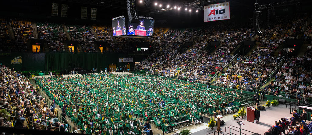 A view of a graduation event from an angle that we can see all of the graduates, the guests seated in the arena seats, and the speaker.