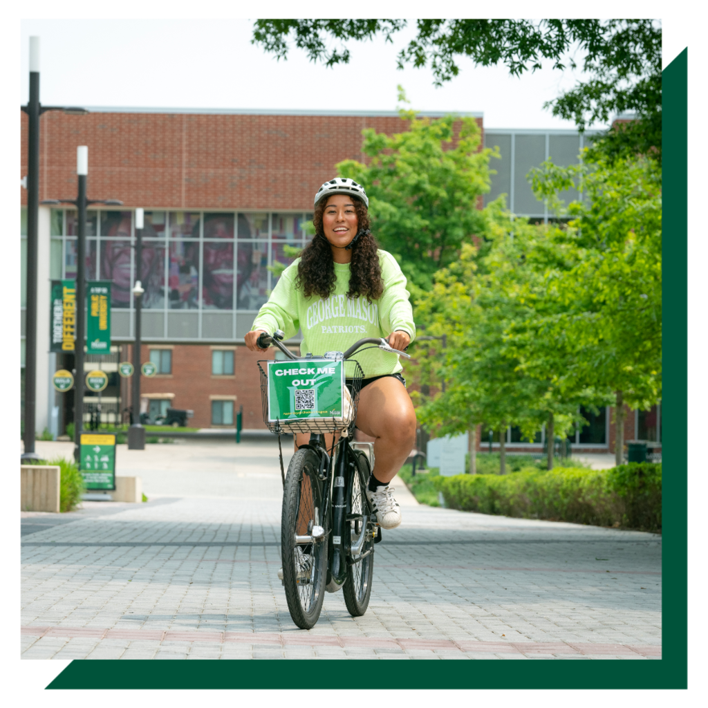 A student smiles and rides a rented bicycle on campus.
