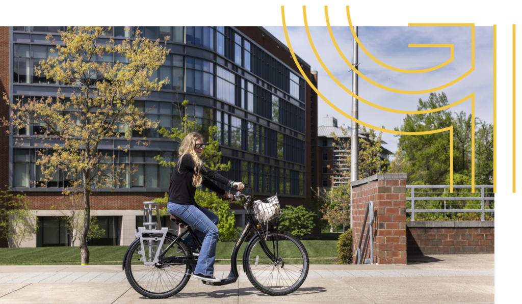 A student rides their bike down the sidewalk outside a building on the Fairfax Campus.