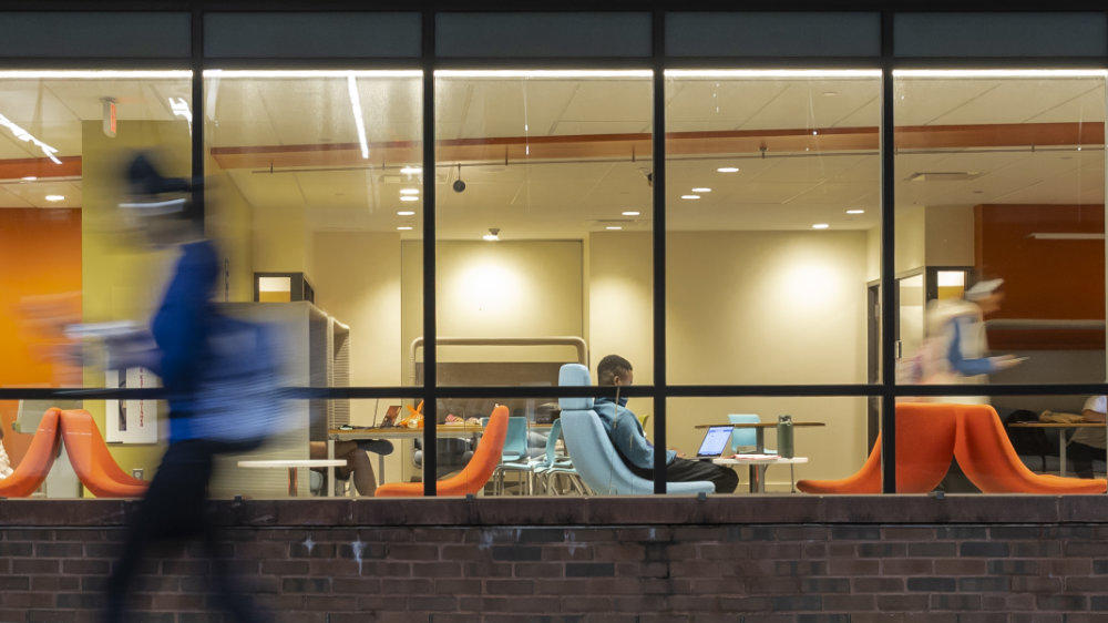 Students study inside Fenwick Library as others walk past outside.