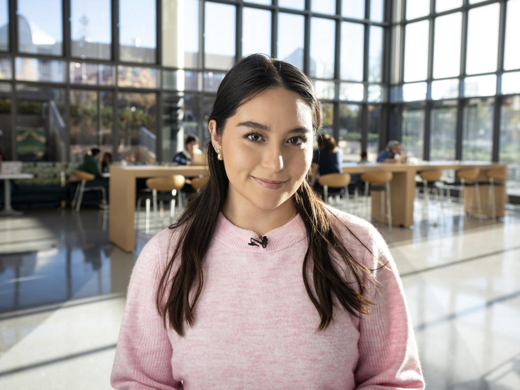 A student stands in the lobby of Horizon Hall. Behind her, students sit at a variety of group tables.