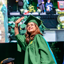 A graduate crossing the commencement stage waves to the crowd.